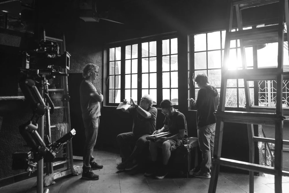 Fotografia em preto e branco de equipe e equipamentos em um ambiente interno de filmagem.